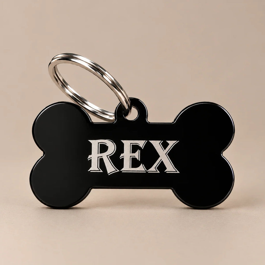 Black bone-shaped stainless steel dog name tag engraved with REX and attached to a silver split ring