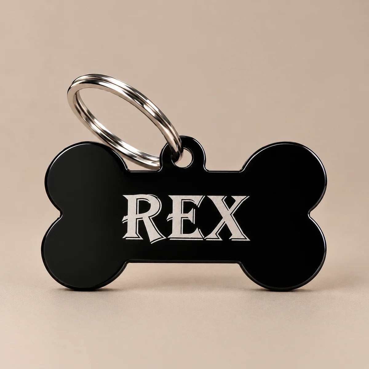Black bone-shaped stainless steel dog name tag engraved with REX and attached to a silver split ring